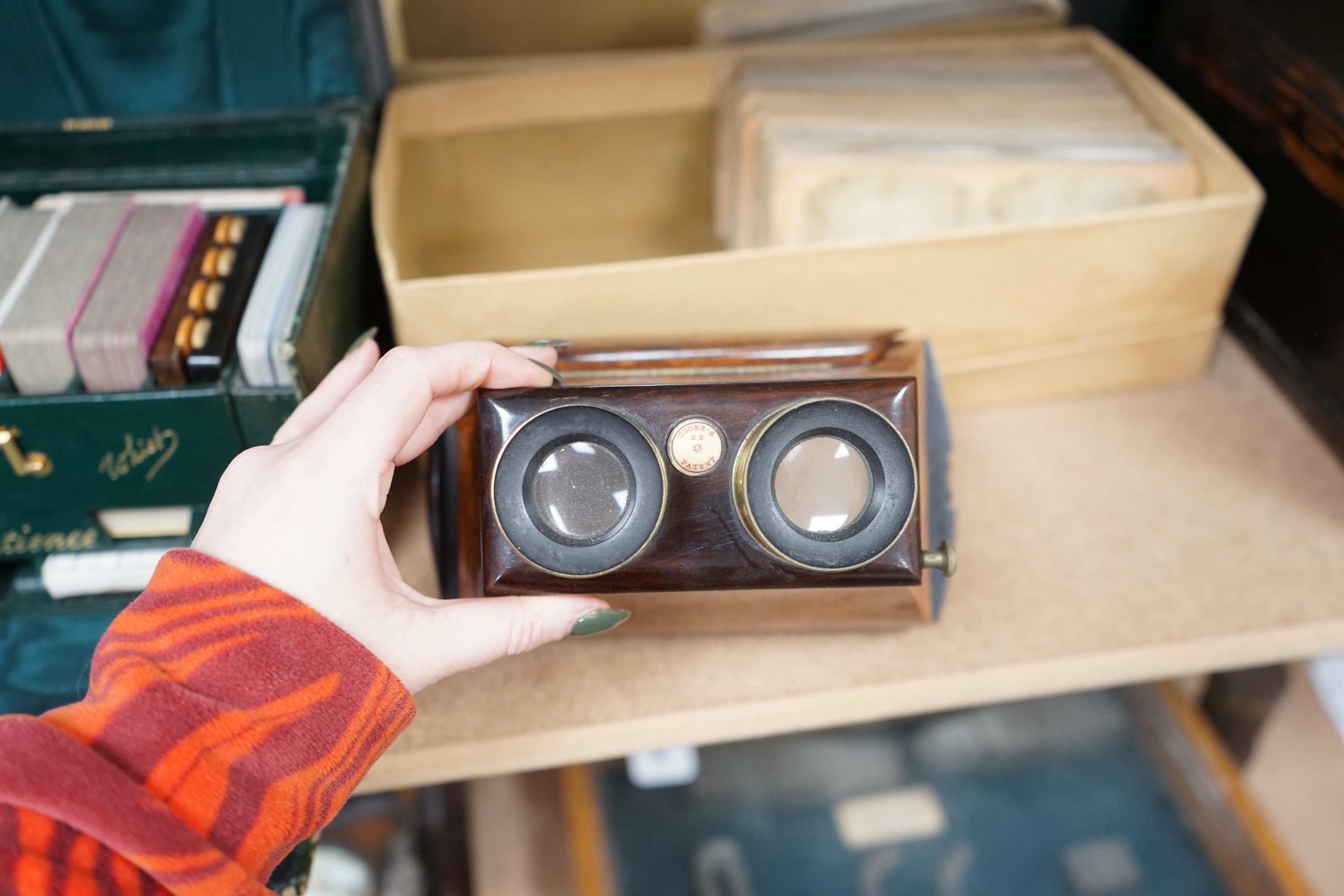 A Cook's patent stereoscope viewer and viewing cards together with a green Morocco leather playing cards box, box 12.5cm high x 24cm wide. Condition, games box poor, viewer and cards good